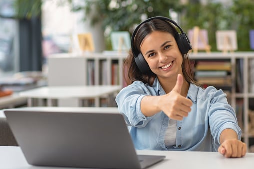 Woman with headphones giving a thumbs up as she takes an online course