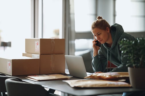 Woman holding a phone and working on a laptop to solve a supply chain problem